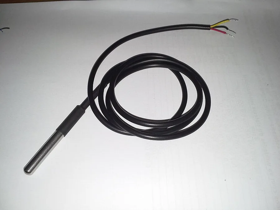 A stainless steel temperature probe about 30 millimetres long on the end of a black two metre lead, coiled on a white sheet of paper. Three bare wires in red, yellow and black are exposed at the far end of the cable.