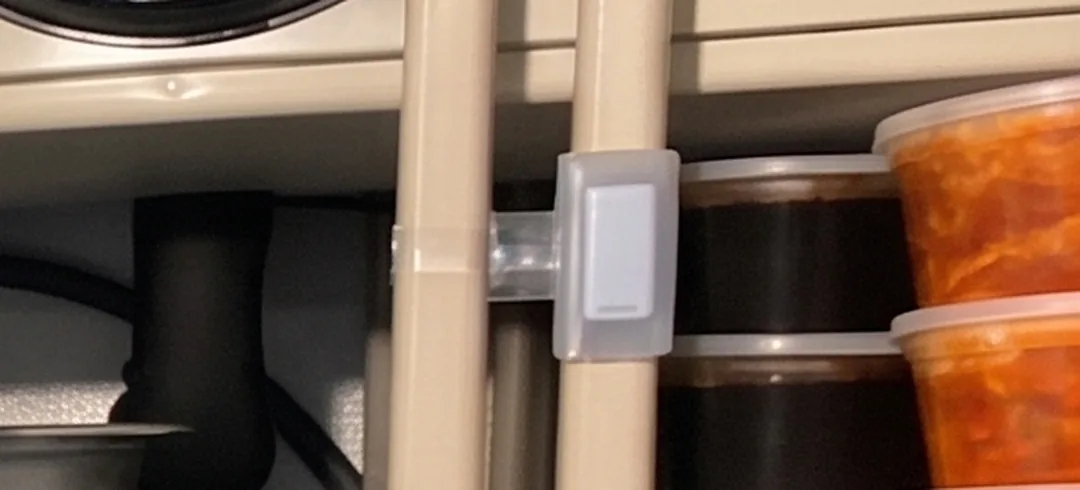 A close view of a TemperatureWise sensor in its bracket on a shelving upright inside a walk-in, with stacked food containers behind it.